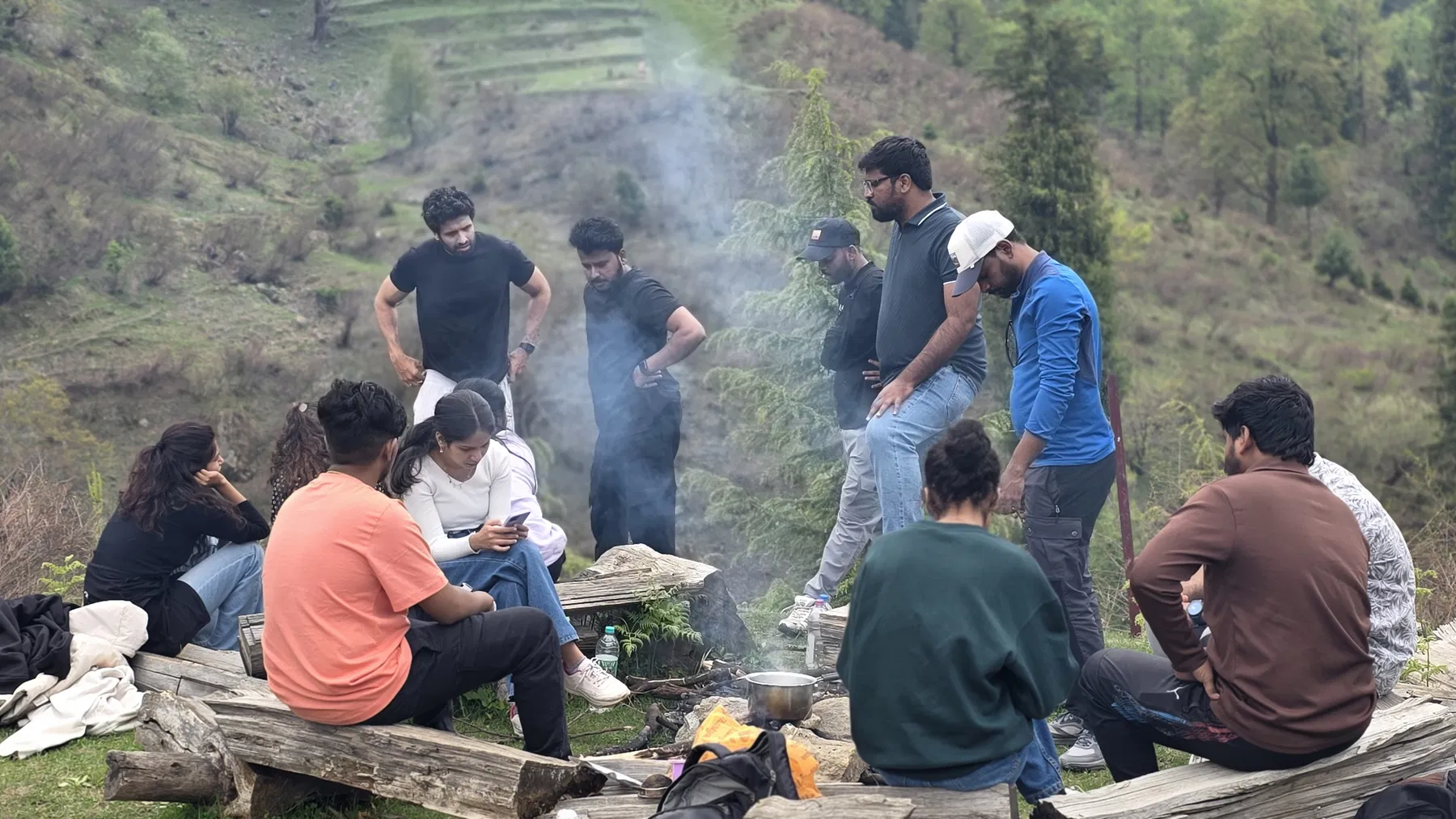 Safar travellers gathered around an outdoor cooking fire on a wooded hillside